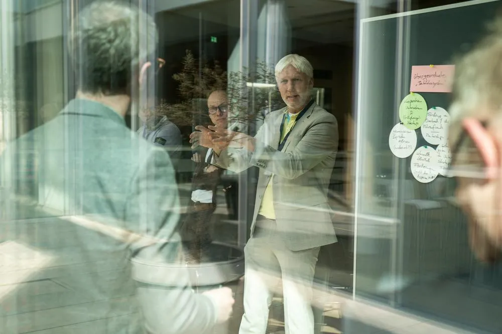 Mehrere Menschen sprechen neben einer Pinnwand miteinander 