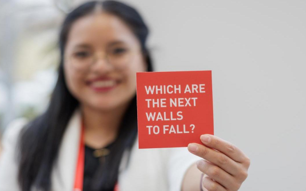 Frau hält eine rote Karte mit der Aufschrift "Which are the next walls to fall?"