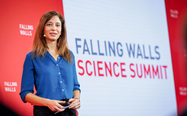 Eine Frau steht vor einem großen Plakat mit der Aufschrift "Falling Walls Science Summit"
