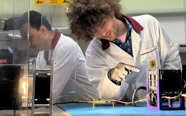 Mann in Laborkittel zeigt auf einen Satteliten