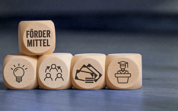 mehrere Würfel mit Symbolen, darunter einer mit der Aufschrift Fördermittel