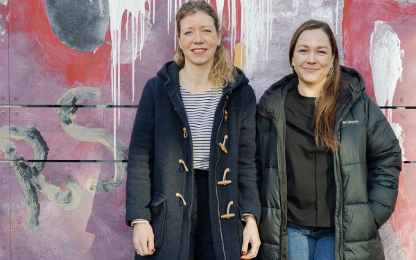 Zwei Frauen stehen nebeneinander vor einer bunten Wand