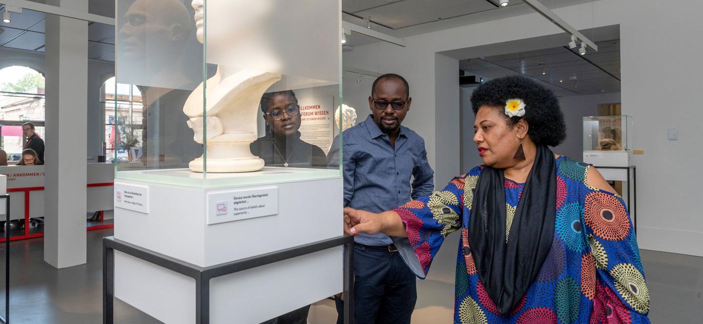 drei Personen stehen um eine Ausstellungvitrine