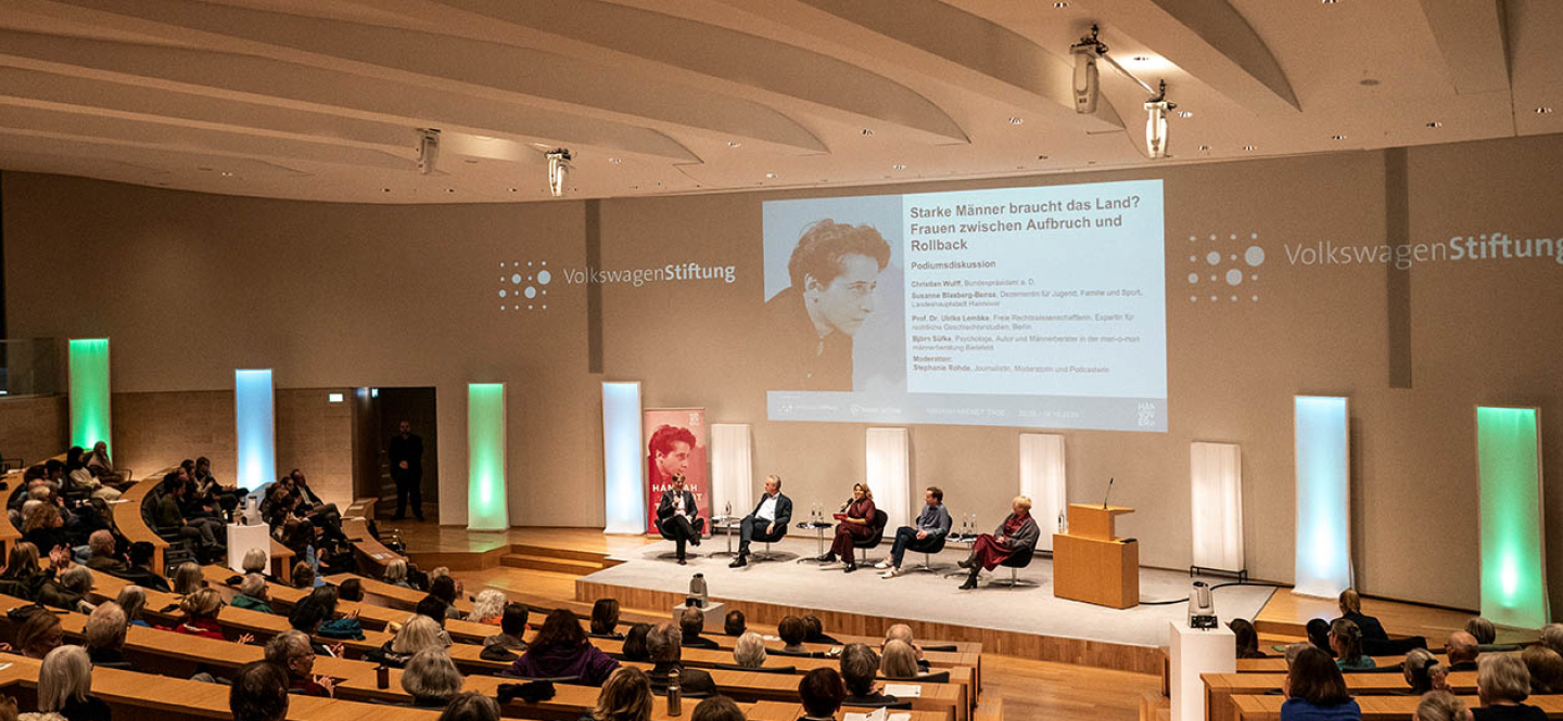Podium mit Gästen im gut besuchten Auditorium