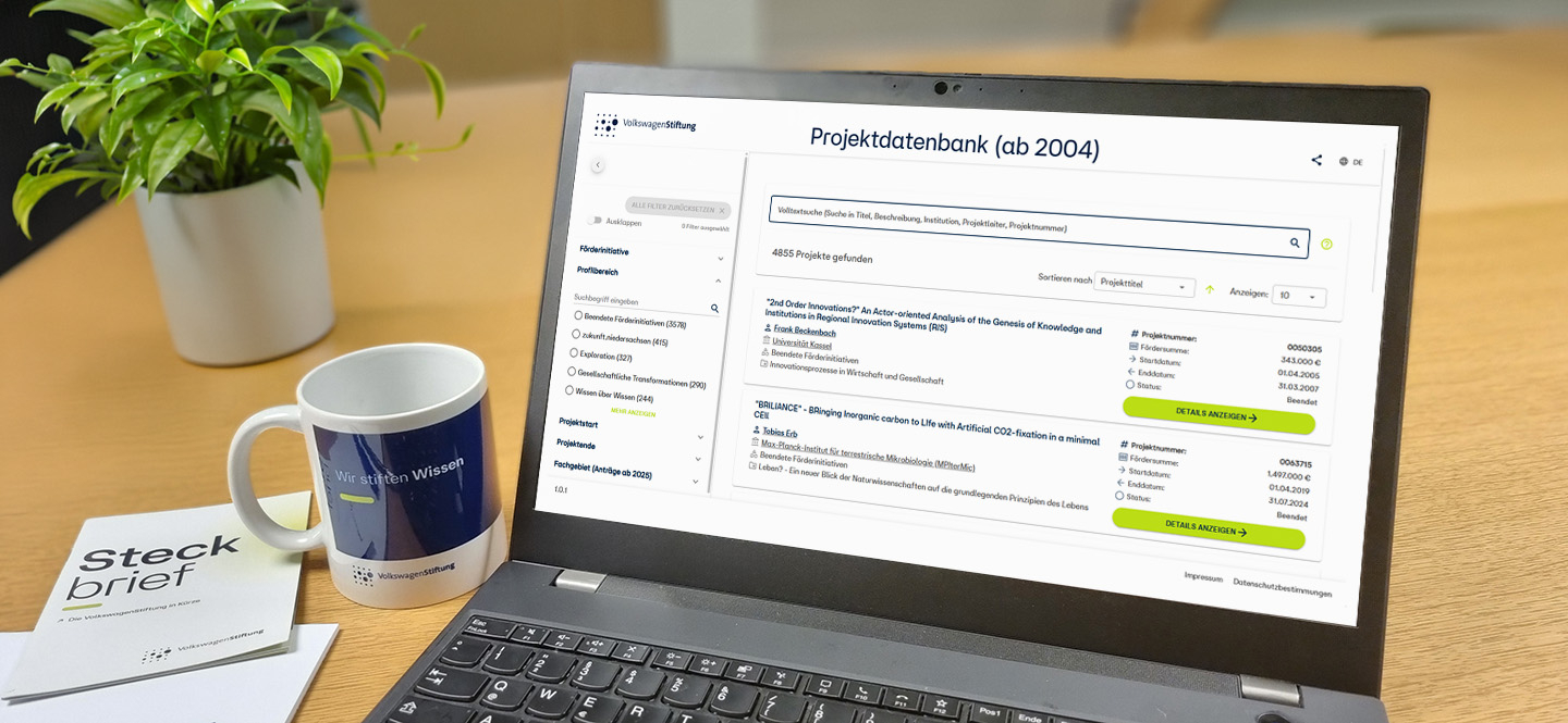 Schreibtisch mit Laptop mit geöffneter Seite "Projektdatenbank", Tasse, Flyer "Steckbrief" und Pflanze