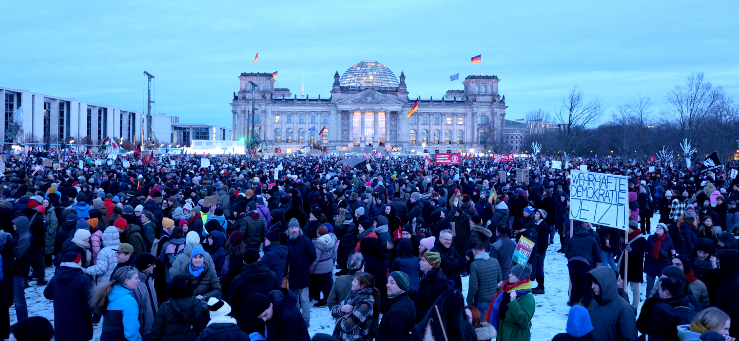 Demonstrierende vor dem Berliner Reichstagsgebäude sind zu sehen, dazu ein Schild mit der Aufschrift "Wehrhafte Demokratie jetzt".