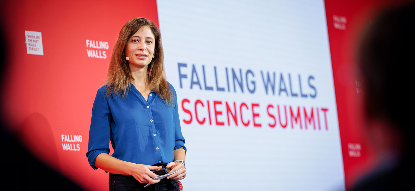 Eine Frau steht vor einem großen Plakat mit der Aufschrift "Falling Walls Science Summit"