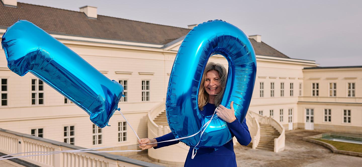Frau mit Luftballon-Zahlen 1 und 0, im Hintergrund Schloss Herrenhausen.