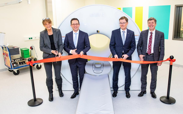 Eine Frau und drei Männer schneiden ein rotes Band durch, das vor einer großen weißen Röhre steht