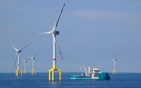 Ein Wartungsschiff fährt an mehreren Offshore Windanlagen in der Nordsee vorbei.