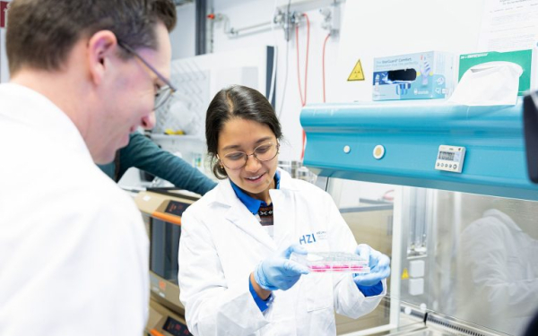 Eine Frau im Kittel vor einem Abzug, in der Hand eine Petrischale