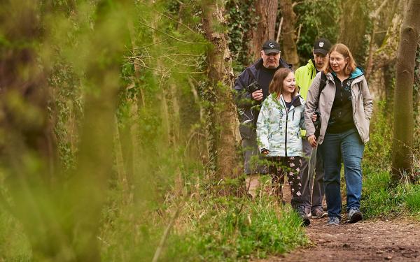 Eine Frau und ein Mädchen laufen vor einenm Mann und einem Jugendlichen durch einen Wald. 