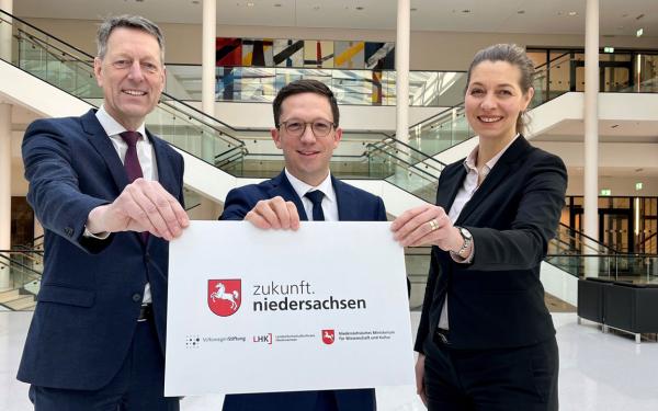 Two men and a woman hold a sign with the imprint "zukunft.niedersachsen" into the camera