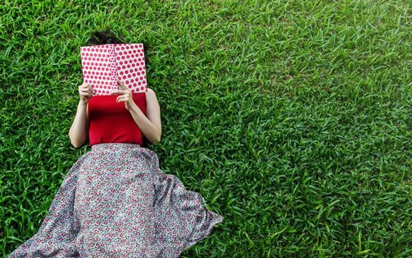 Eine Frau liegt auf einer Wiese und liest ein Buch.