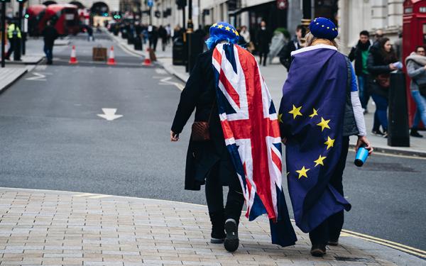 Zwei Menschen laufen durch eine Straße. Einer trägt den Union Jack, einer eine Europa-Flagge.