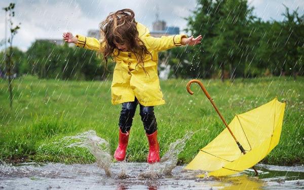 Mädchen in Regenkleidung spielt gut gelaunt in Pfütze 