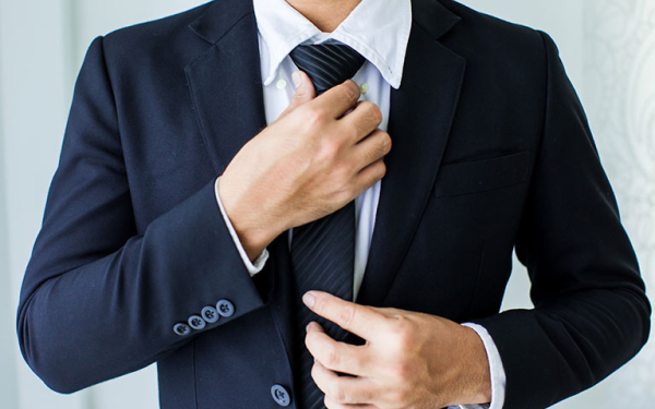 Das Bild zeigt den Oberkörper eines Mannes in Hemd und Sakko, der sich den Krawattenknoten festzieht. n