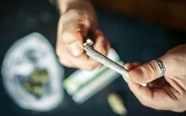 Das Bild zeigt zwei männliche Hände von oben. Eine hält einen Joint, die andere zündet ihn an. 