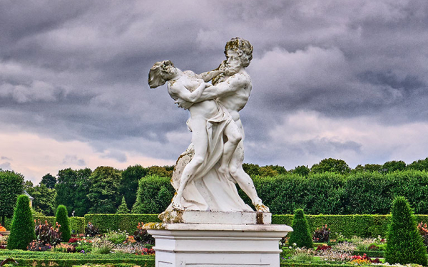 Das Bild zeigt zwei Sandsteinskulpturen im Großen Garten Herrenhausen vor einem wolkenbehangenen Himmel