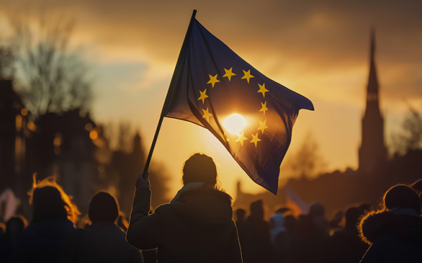 Das Bild zeigt eine EU-Flagge hinter der die Abendsonne durchscheint.