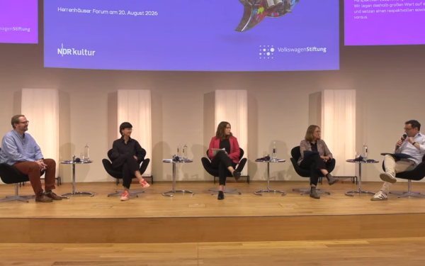 Ein Podium aus fünf Menschen sitzt auf einer Bühne und spricht miteinander