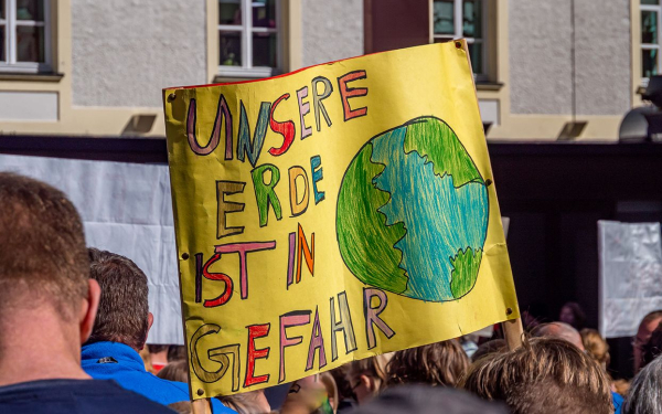 Das Bild zeigt den Ausschnitt aus einer Klimademonstration mit einem Transparent auf dem "Unserer Erde ist in Gefahr" steht.