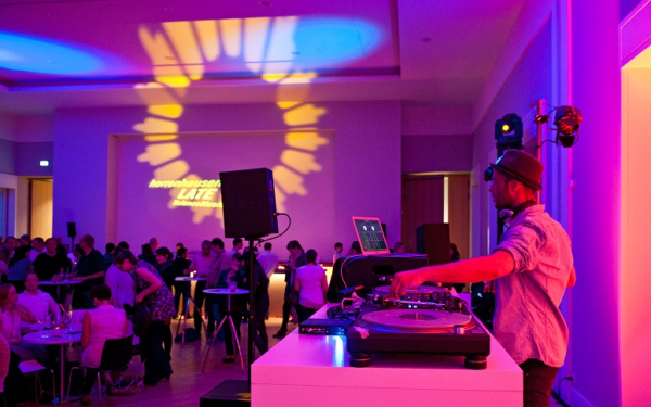 Das Bild zeigt eine Szene mit DJ und Publikum in loungiger Atmosphäre