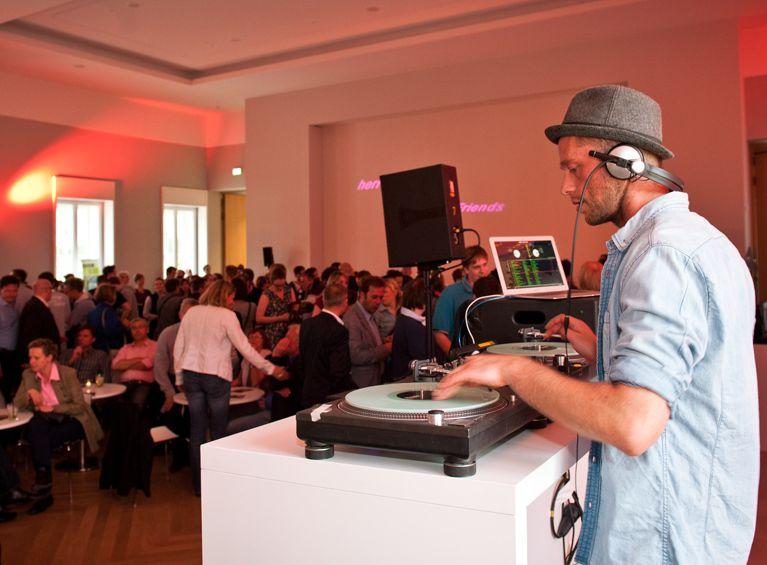 Das Bild zeigt einen DJ in einem bunt beleuchteten Veranstaltungsraum