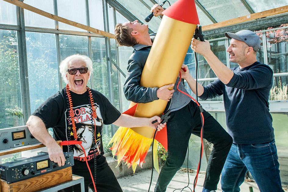 drei Männer in Rocker-Kleidung, einer davon mit Raketen-Attrappe