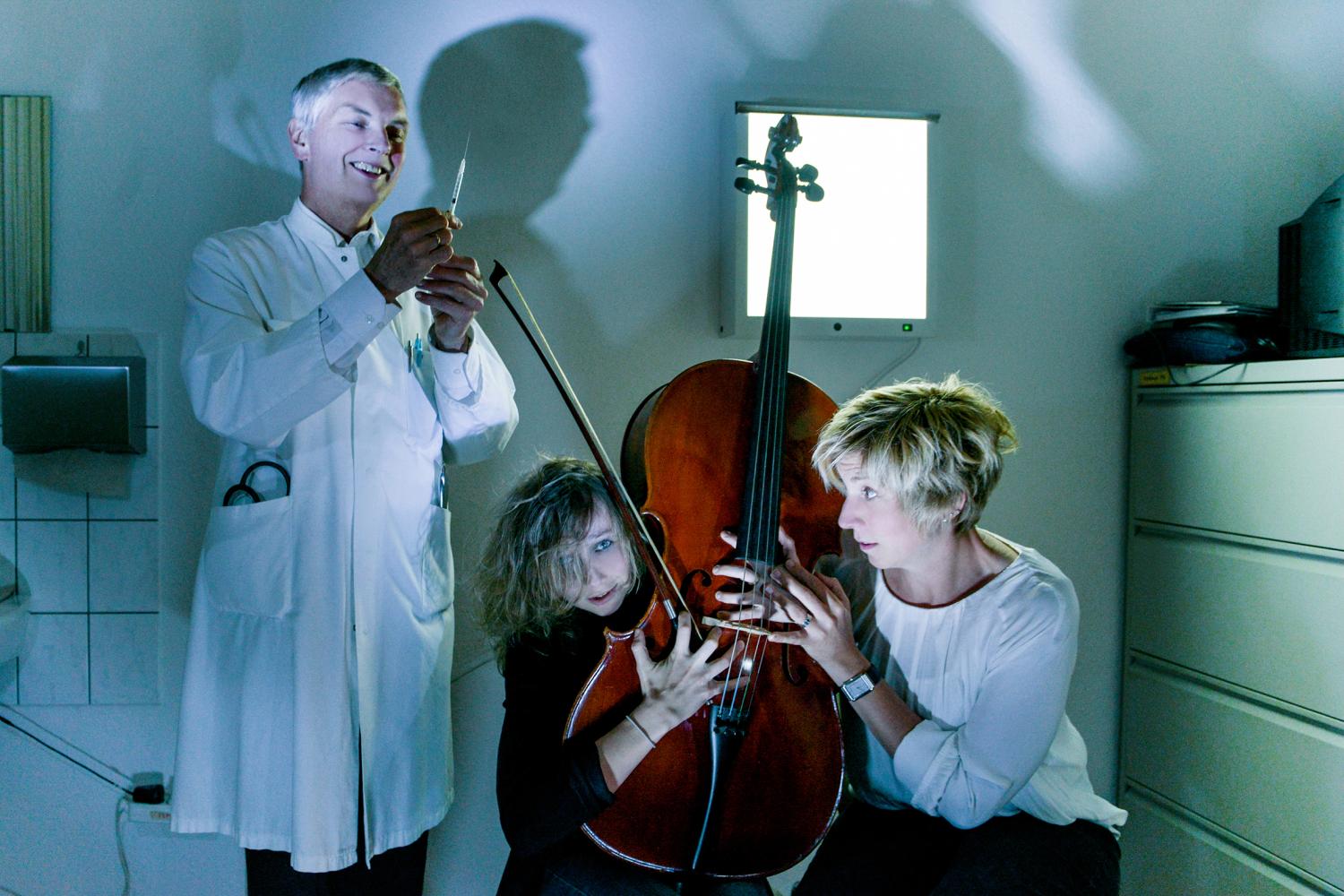 lachender Mediziner mit Spritze, daneben zwei kauernde Frauen mit einem Cello