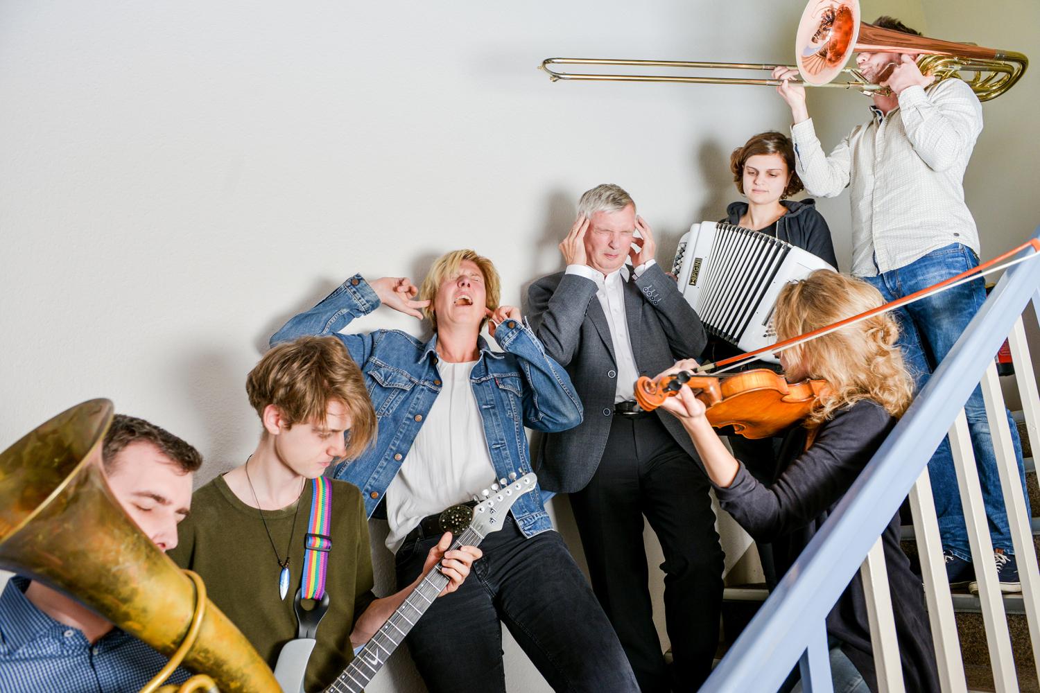 Musiker mit verschiedenen Instrumenten auf einer Treppe, ein Mann hält sich die Ohren zu