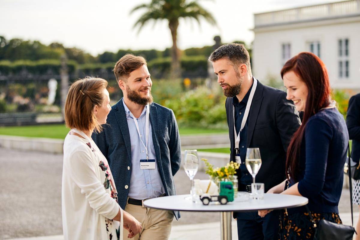 zwei Männer und zwei Frauen mit Konferenzbadge an einem Stehtisch vor dem Tagungszentrum Schloss Herrenhausen