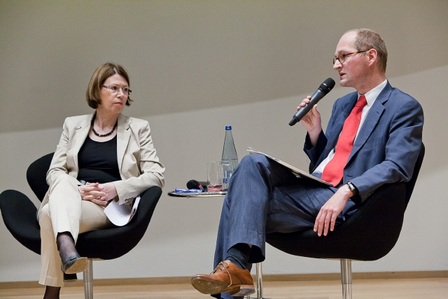 Podium mit zwei Personen, einer davon spricht in ein Mikrofon
