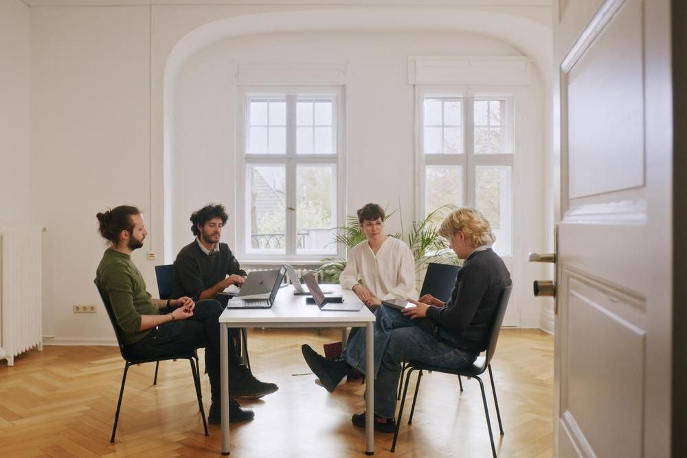 Eine Gruppe von vier Menschen sitzt um einen Tisch und bespricht sich
