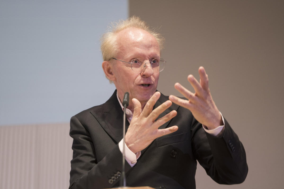 Mann spricht in ein Mikro und gestikuliert dabei