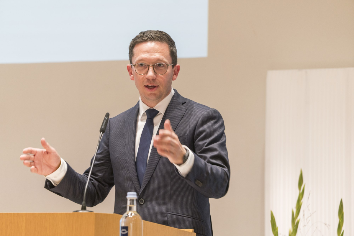 Mann gestikuliert mit den Händen während er am Pult steht und spricht