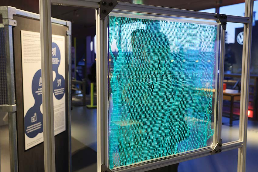 Ein türkises Fischernetz ist in einem durchsichtigen Schaukasten aufgespannt.