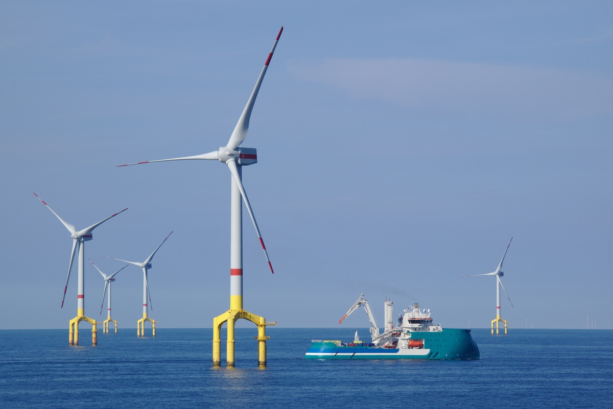 Ein Wartungsschiff fährt an mehreren Offshore Windanlagen in der Nordsee vorbei.