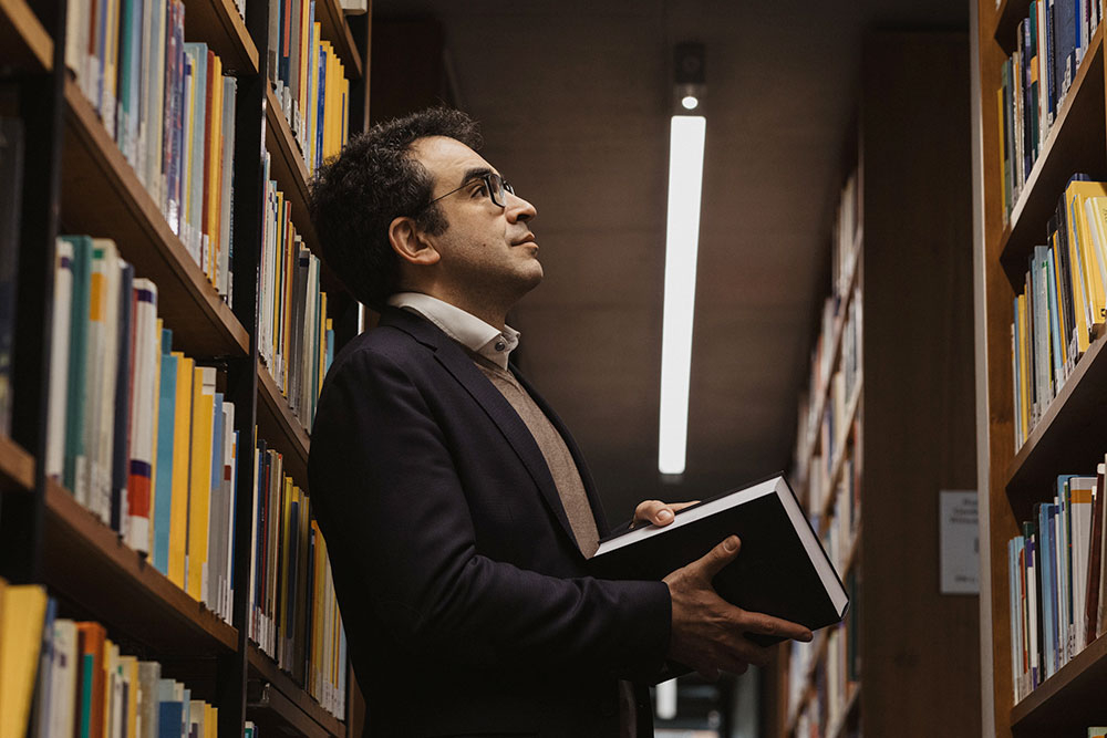 Ein Mann hält ein Buch und steht in einer Bibliothek