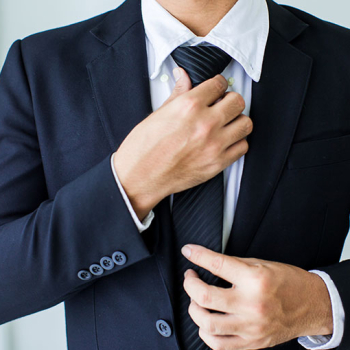 Das Bild zeigt den Oberkörper eines Mannes in Hemd und Sakko, der sich den Krawattenknoten festzieht. n