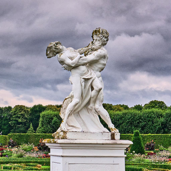 Das Bild zeigt zwei Sandsteinskulpturen im Großen Garten Herrenhausen vor einem wolkenbehangenen Himmel