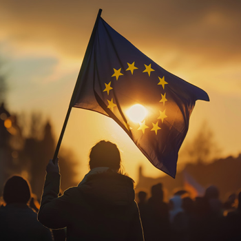 Das Bild zeigt eine EU-Flagge hinter der die Abendsonne durchscheint.