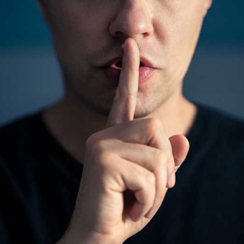 Ein Mann macht eine "Psst"-Geste und hält sich dafür den Zeigefinger vor den Mund.