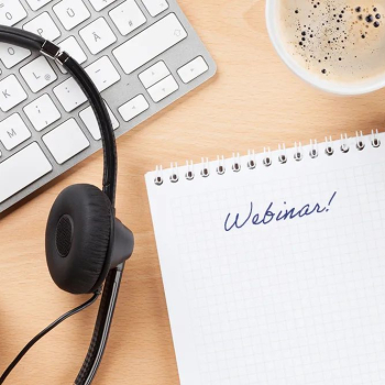 Tastatur, Kopfhörer, Kaffeetasse, Stift und Block mit Aufschrift "Webinar!"
