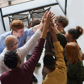 Zu sehen sind eine Gruppe erfolgreicher junger Menschen, die gemeinsam in ihrer Mitte die Arme empor strecken. 