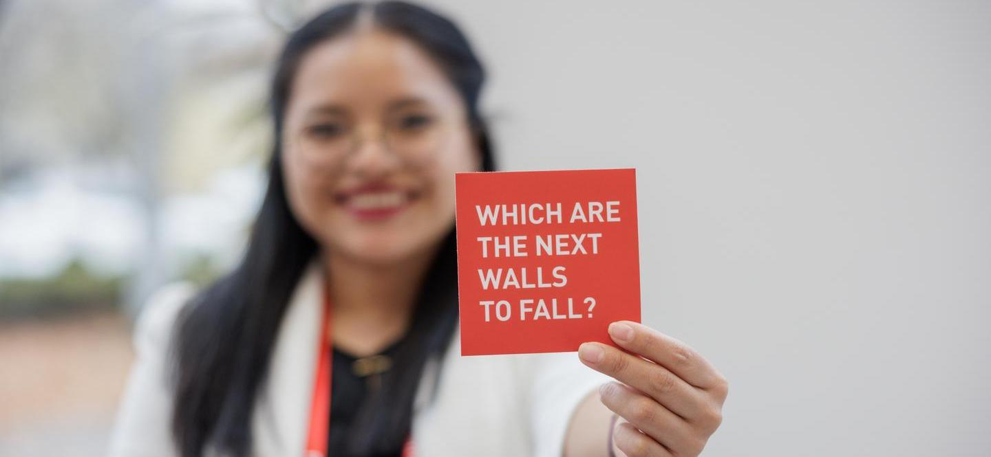 Frau hält eine rote Karte mit der Aufschrift "Which are the next walls to fall?"