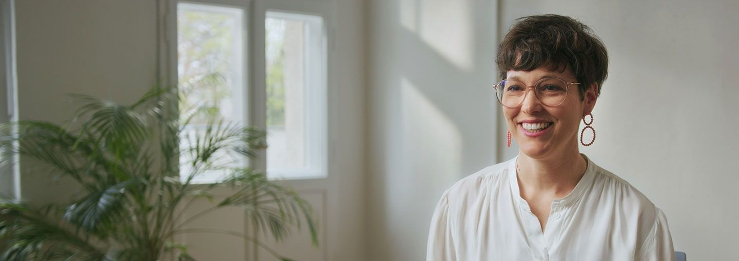 Frau mit Brille in weißer Bluse lächelt in Kamera