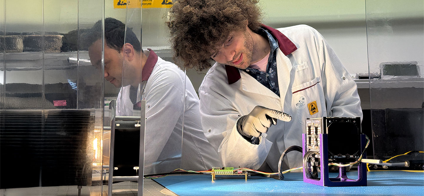 Mann in Laborkittel zeigt auf einen Satteliten