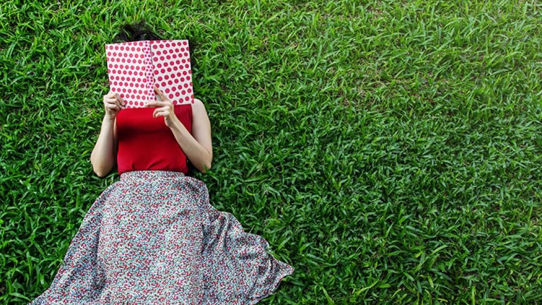 Eine Frau liegt auf einer Wiese und liest ein Buch.