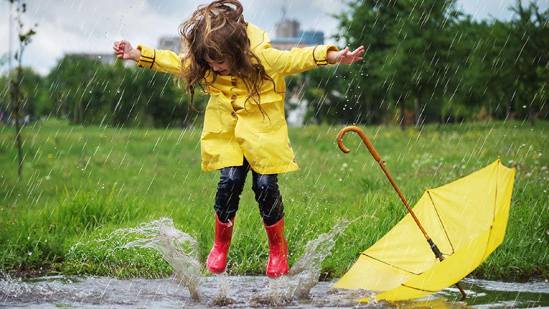 Mädchen in gelbem Regenmantel springt in Pfütze